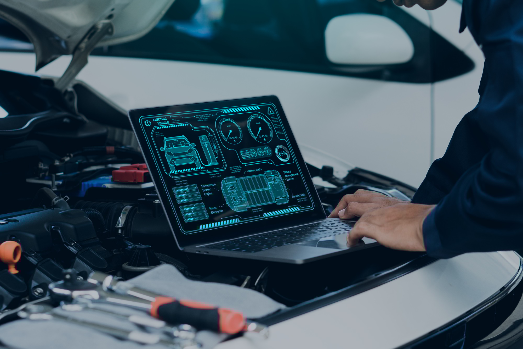 Car mechanic using laptop computer examining tuning fixing repairing car engine in garage.